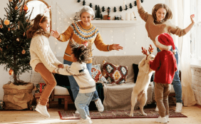 Eine Familie tanzt vor einem Weihnachtsbaum zusammen mit dem Familienhund