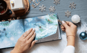 Aufgeschlagenes Buch "My frozen Memories" im weihnachtlichen Setting passend zum Buchcover, Hände schneiden mit Brieföffner die Seiten auf