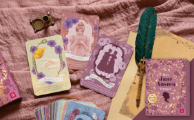 Nahaufnahme von "Das Jane Austen Orakel" mit mehreren gezogenen, illustrierten Orakelkarten, einer Feder und einem Buch auf einem rosa Tuch.
