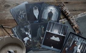 Stimmungsbild zu den Orakelkarten "Erdenkind" mit verschiedenen mythischen Figuren, Räucherwerk und blauer Tischläufer auf Holztisch