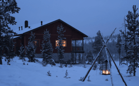 Verschneites rustikales Haus in der Abenddämmerung, draußen und drinnen brennt ein Licht, gemütliche ruhe Atmosphäre