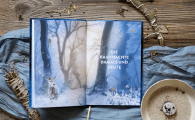 Aufgeschlagenes Buch mit Doppelseite im winterlichen Wald auf mystischen Hintergrund. Es ist Räucherwerk und eine Brennschale zu sehen auf einem blauen Tischläufer