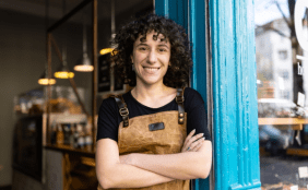 Inhalberin steht mit Lächeln und verschränkten Armen im Türrahmen ihres Cafes