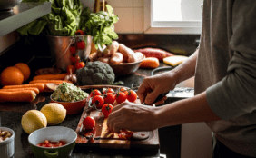 Person steht vor dem Küchentresen, auf dem ganz viel Gemüse liegt, das geschnitten wird.