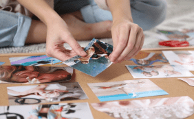 Nahaufnahme von Händen, die verschiedene persönliche Fotos mit Pinnnadeln an einer Korkpinnwand befestigen.