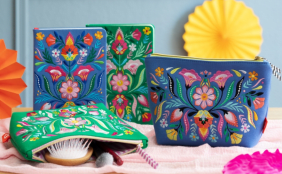 Bestickte Notizbücher in grün und königsblau mit floralem Muster, dazu passend zwei Accessoirestaschen in den gleichen Farben und Designs. Zusammen fotografiert in einem farbenfrohen Ambiente mit bunten Papierrosetten dekoriert