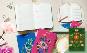 erminkalender 2027 aufgeschlagen, umgeben von drei kleinen Notizbüchern mit aufwendigen Blumen- und Vogelstickereien.
