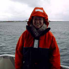Unsere Lektorin Anne auf einem Boot mit orangener Regenjacke, sie lächelt in die Kamera