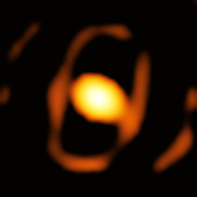 Verschwommene Aufnahme eines Sterns kurz vor der Explosion zur Supernova. In der Mitte ein heller, gelber Kreis, umgeben von einem gelblichen Schatten in Form einer Acht, dazwischen schwarzer Hintergrund.