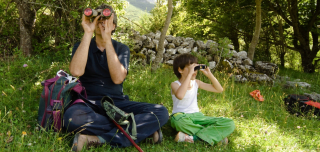 Papa und Kind mit Fernglas auf einer Wiese vor einem Wald