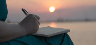 Frau schreibt in ihr Tagebuch während des Sonnenuntergangs