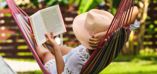 Frau liegt in einer Hängematte im Garten und liest ein Buch