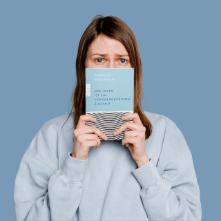 Eine Frau im grauen Pullover hält «Das Leben ist ein vorübergehender Zustand» von Gabriele von Arnim vor den Mund