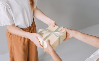 erwachsene Hände übergeben eine gelbe Geschenkbox an Kinderhände