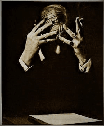 Der Autor Paul Valéry im Anzug; den Kopf in die Hände gestützt, grübelt er über einem Blatt Papier das vor ihm auf einem Tisch liegt.
