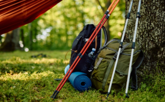 Rucksack, Wanderstöcke, Isomatte und Hängematte im Wald zum Thema Camping Essentials