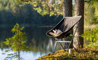 ein buch auf klappstuhl am see zum thema camping essentials