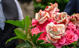 Mann im Anschnitt hält einen Blumenstrauß mit Geldscheinen, die zu Rosen gefaltet sind