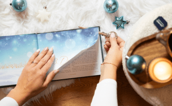 Aufgeschlagenes Buch "Das Geheimnis von Asfjördur" in weihnachtlichem Ambiente passend zum Buch, eine Hand schneidet mit einem Brieföffner die Seiten auf