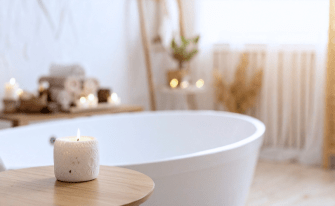 Entspannende Badeszene mit angezündeter Kerze im Vordergrund und einer freistehenden Badewanne im Hintergrund.