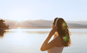 Eine Frau mit Kopfhörern lauscht Musik bei Sonnenuntergang über einem Gewässer.