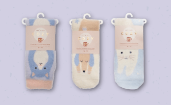 Drei Paar flauschige Couch-Socken in ihrer Verkaufsverpackung mit der Aufschrift „Let's get cozy – Couch-Flauschsocken“. Die Socken zeigen niedliche Tiermotive: links eine Katze auf blau-rosa Hintergrund, in der Mitte ein schlafender Hund auf Cremeweiß und rechts eine weiße Katze auf Hellblau.