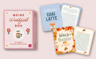 Eine rosa gestaltete Box mit dem Titel „Meine Wohlfühlbox – 50 Impulse für mehr Gemütlichkeit“. Rechts daneben liegen vier Beispielkarten, darunter Rezept- und Ideenkarten wie „Wärmendes Chai Latte“ oder „Waldbaden für zu Hause“ mit herbstlichen Blätter-Illustrationen.