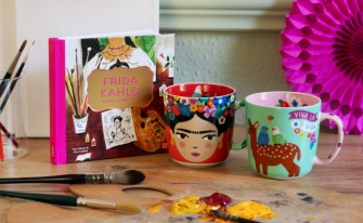 Künstlerisches Setting mit Pinseln, Leinwänden und Malpalette mit Farben. Platziert sind das Buch "Frida Kahlo - Ein Leben in allen Farben", sowie die beiden Tassen mit verschiedenen Frida Kahlo - Designs.