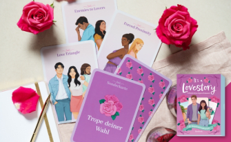 Produktbild des Kartenspiels „It's a Love Story“ von Pattloch. Die lila Verpackung ist unten rechts zu sehen. Auf einer hellen Unterlage sind verschiedene illustrierte Karten mit Romance-Themen wie „Love Triangle“, „Enemies to Lovers“, „Forced Proximity“ und eine lila Sonderkarte („Trope deiner Wahl“) aufgefächert. Dekoriert ist die Szene mit zwei frischen rosa Rosen, Blütenblättern und einem Notizbuch mit goldenem Stift.