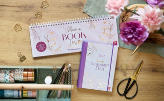 Wochenplaner 'I believe in Book Love' und Buch 'In my Romance Era' auf Holzschreibtisch mit Stiften und Schere.
