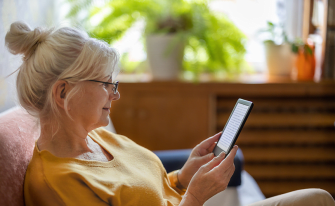 Frau sitzt mit E-Reader in der Hand auf Couch