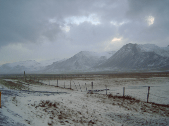 Winterszene auf Island, im Hintergrund Berge, im Vordergrund Weideland mit leichtem Schnee