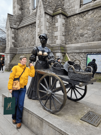 Bronzestatue von Molly Malone, die einen Handwagen auf zwei Rädern schiebt, au fdme sich geflochtene Körbe liegen