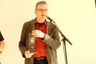 Klaus N. Frick mit dem BuCon-Ehrenpreis in der Hand vor einem Mikrofonständer.