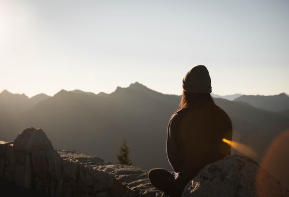 Eine Frau sitzt auf einem Berggipfel und sieht in die Ferne