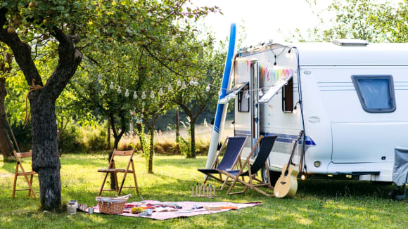 camping-essentials-wohnwagen-auf-wiese-mit-stühlen