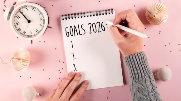 Draufsicht auf eine Hand in einem grauen Strickpullover, die mit einem weißen Stift die Überschrift 