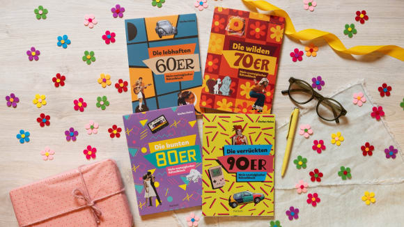 Die vier Rätselhäfte mittig angeordnet, drumherum kleine bunte Filzblümchen, eine Brille und Stift und ein kleines Geschenk. Liegt alles auf einem hellen Holzboden.