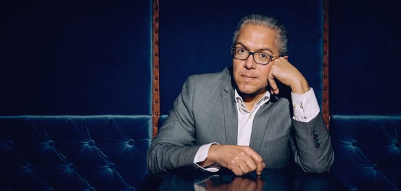 Steffen Kopetzky sitzt an einem Tisch, stützt den Kopf auf eine Hand und schaut in die Kamera