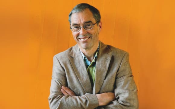 Friedemann Schulz von Thun steht mit verschränkten Armen vor einer Wand und lächelt in die Kamera