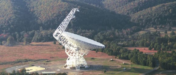Das Greenbank-Teleskop. Ein großes Radioteleskop, dass in einer von Bäumen umgebenen Landschaft steht.