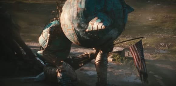 Riesiger Animatronik-Roboter in Disney typsicher Tiergestalt sitzt mit hängendem Kopf vor dem United States Marine Corps War Memorial, in der linken Hand die US-Flagge, die sonst die Soldaten gemeinsam hochhalten.