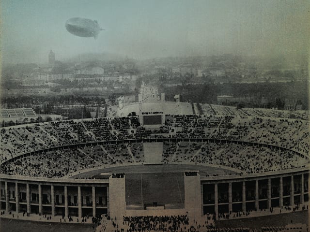 Ein Olympiastadion in Deutschland zur NS-Zeit mit einem am Himmel fliegenden Zeppelin