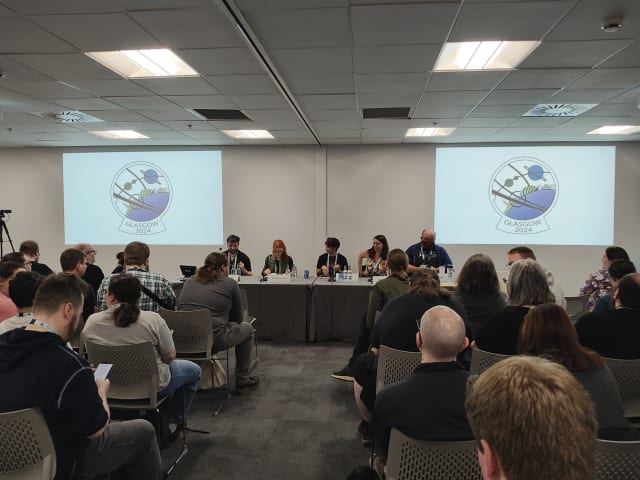 Ein Panel in einem kleineren Raum, mehrere Menschen sitzen an einem langen Tisch, gegenüber dem Publikum