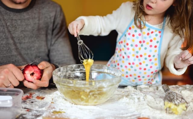 Kind und Elternteil beim Kochen, Kind rührt Teig mit Schneebesen