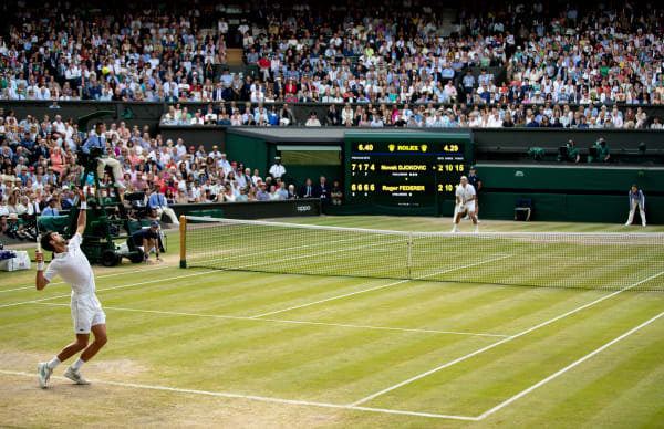 A man dressed in white preparing to serve in a tennis match at Wimbledon.