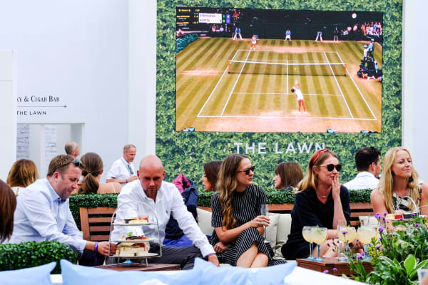 People sitting in a bar on comfortable seats with a tennis match playing on a screen behind them.