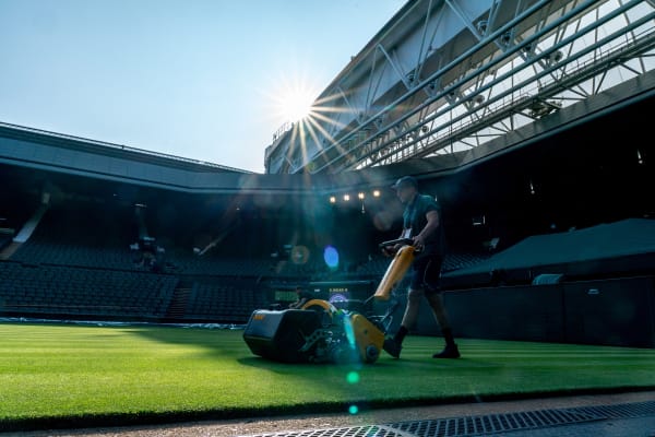 Person in navy outfit mowing the grass in the early morning at Wimbledon.