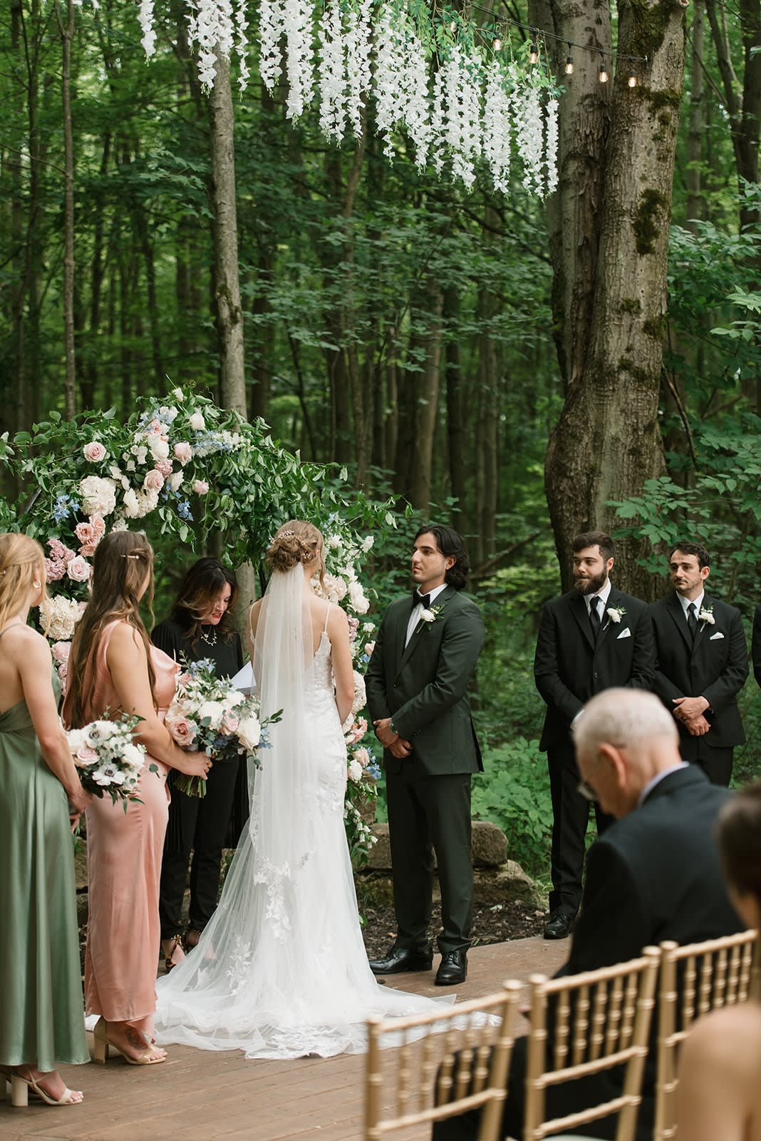 Bride and groom exchanging vows at a floral arch in a woodland setting at Sugar Lake Weddings