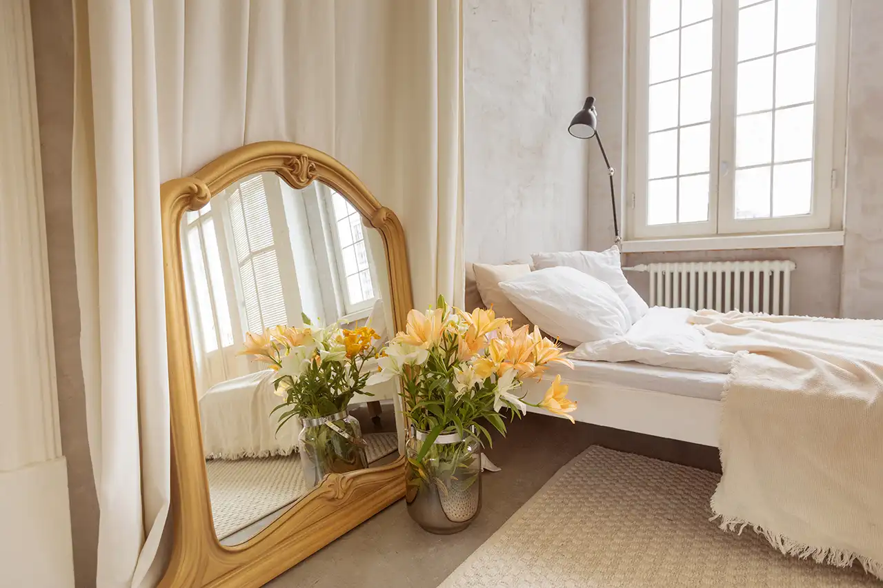 Elegantly staged minimalist bedroom with mirror and flower arrangement on floor